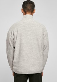 Lys grå strikket sweater med høj krave, der har et tekstureret mønster samt ribbede manchetter og kant. Konstrueret af bæredygtigt materiale.