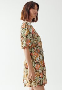 Floral dress with short puff sleeves, cinched waist, and relaxed fit. Features a brown base with vibrant orange, green, and white patterns.