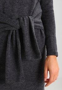 Abito a maglia grigio scuro a coste con una ampia cintura legata in vita, maniche lunghe e una texture morbida.