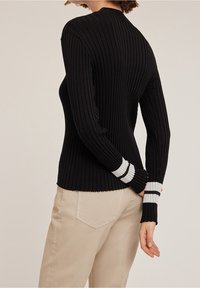 Czarny sweter prążkowany, z długimi rękawami, z białymi i szarymi paskami na mankietach. Gładka tekstura, dopasowany krój.