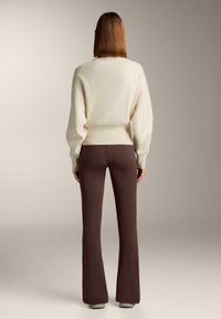Crèmekleurige oversized trui met een ontspannen pasvorm en geribbelde zoom, gecombineerd met bruine uitlopende broek, met een gladde textuur en strakke lijnen.