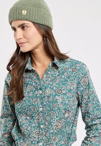 Grünblumiges Button-Down-Hemd mit einem gemusterten Design; ausgestattet mit einer gerippten grünen Mütze, die vorne ein dekoratives Anker-Patch hat.
