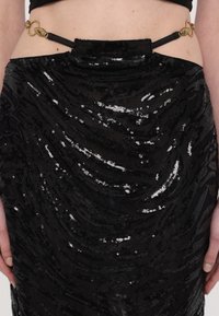 Black sequin skirt featuring a wavy texture, an elastic waistband, and a decorative gold hardware detail at the back.