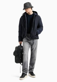 Doudoune bleu marine, sweat à capuche noir, jeans gris, baskets noires avec semelle crème, chapeau seau gris, sac à dos noir avec des accents texturés.