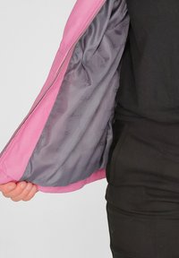 Rosa Jacke mit glatter Außenseite und grauem Satin-Innenfutter. Verfügt über einen Reißverschluss und eine sanfte Textur. Offen, um das Innenfutter zu zeigen.