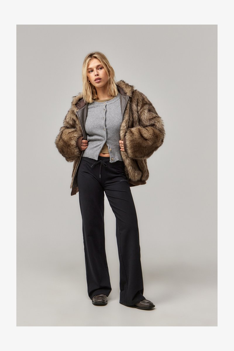 Braune Kunstfell-Übergröße-Jacke mit einem grauen, geknöpften Oberteil und schwarzen, weiten Hosen. Glatte Textur, lockere Passform und neutrales Farbschema.