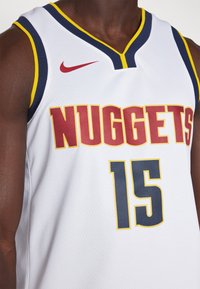 Biely basketbalový dres s červeným a žltým textom "NUGGETS", veľkým námorníckym číslom "15" a červeným logom Nike na štruktúrovanej tkanine.