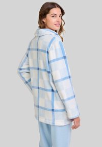Chaqueta de forro polar a cuadros en azul claro y blanco, con cuello, textura suave, mangas largas y bolsillos laterales, llevada sobre pantalones azul claro.