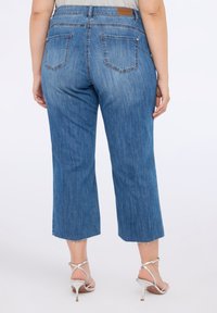 Pantalones cortos de mezclilla azul con dobladillo deshilachado, cinco bolsillos y un ligero desgastado. Colocados sobre un fondo liso, que destaca las características del diseño.