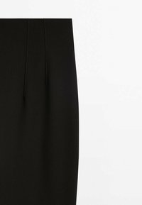 Jupe crayon noire taille haute avec des détails de coutures verticales sur un tissu lisse sur fond blanc.
