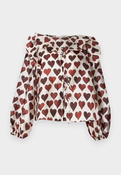 Μπλούζα με μακριά μανίκια, γυαλιστερή, με κόκκινα μοτίβα καρδιών, με γιακά με βολάν και δέσιμο εμπρός σε λευκό φόντο.