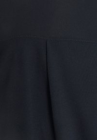 Tissu bleu marine foncé avec une couture horizontale et un pli central, montrant la texture et les détails de couture sur un vêtement.