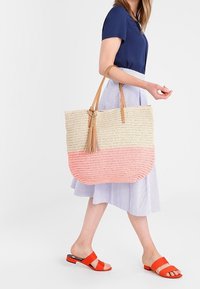 Vävd tote-väska med en beige överdel och en rosa nedre del, läderhandtag med en tofsdetalj och en rundad bottendesign.