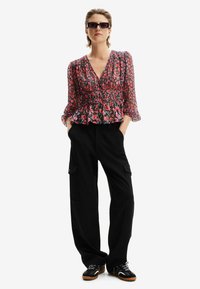 Blusa floreale, leggera, con vita arricciata, caratterizzata da motivi rossi, rosa e verdi. Abbinata a pantaloni cargo neri larghi e sneakers nere.