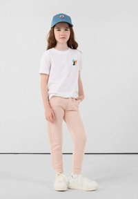 Witte t-shirt met kleurrijk logo, lichtroze sweatpants en blauwe pet. Witte sneakers maken de casual outfit compleet. Eenvoudig en functioneel ontwerp.