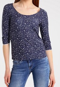 Marineblaue Bluse mit drei Viertelärmeln und weißen Punkten. Hergestellt aus weichem Stoff mit einem Rundhalsausschnitt und subtilen strukturierten Akzenten.