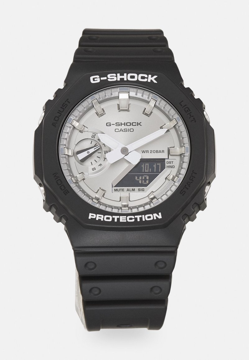 Montre-bracelet G-SHOCK avec un boîtier et un bracelet en résine noire, un cadran argenté avec des affichages analogiques et numériques, et un texte blanc pour les étiquettes de fonction.