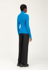 Maglione a colletto alto in maglia a coste blu vivace, abbinato a pantaloni neri a gamba larga e stivali neri robusti. Tessuto strutturato con dettaglio sul retro.