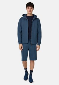 Sudadera deportiva azul oscuro con cremallera frontal y dos bolsillos, combinada con pantalones cortos a juego. Cuenta con mangas cortas y cintura ajustable con cordón.