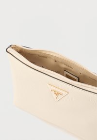 Μπεζ θήκη καλλυντικών με υφή στο υλικό, κλείσιμο με φερμουάρ στην κορυφή και τριγωνικό λογότυπο σε χρυσή απόχρωση. Το εσωτερικό διαθέτει φόδρα με επωνυμία.