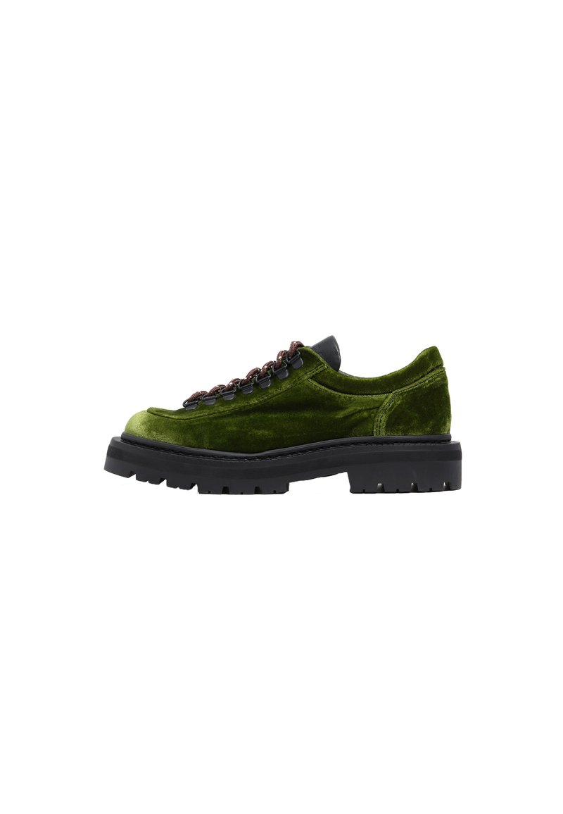 Zapato deslizante de terciopelo verde con suela de goma negra, que presenta un detalle de cadena marrón en la parte superior y acentos de textura suave.