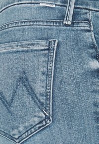 Denimfarkut, joissa on vaalea sininen pesu, erottuva takatasku, jossa on sahalaitakuviota, ja kontrastivärinen ompelu reunoilla.