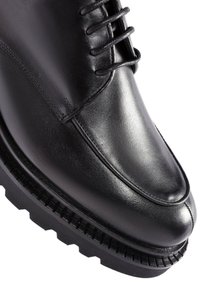 Schwarzer Lederschuh mit runder Zehenform, Schnürung vorne, glatter Oberfläche und einer strukturierten Gummisohle mit Rillen. Keine sichtbaren Muster oder Akzente.