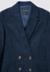 Blazer doppiopetto in corduroy blu navy con due tasche frontali, rever a lancia e bottoni in tono argento. L'interno foderato è visibile.