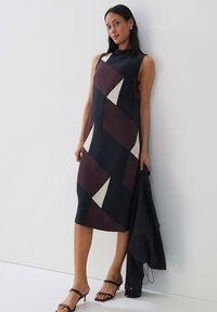 Ärmelloses, farblich unterteiltes Kleid in Marineblau, Burgunderrot und Creme mit geometrischen Mustern. Der Stoff hat eine glatte Textur; knielanges Design.
