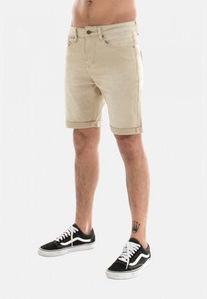 Shorts en denim beige avec une coupe décontractée, ourlets retroussés et poches avant. Associés à des baskets noires avec des accents blancs et des lacets.