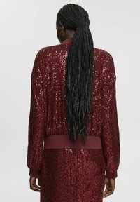 Burgundy rhinestenson bomberjakke med ribbet cuff og søm, der har en tekstureret overflade og en løs pasform, set fra bagsiden.