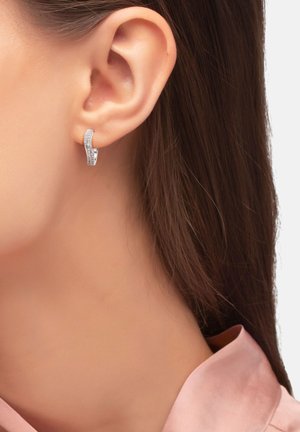 Orecchini d'argento con un design curvo, caratterizzati da una fila di pietre preziose trasparenti su un lato, attaccati all'orecchio. Texture liscia e finitura lucida.