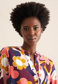 Blusa colorata con motivo floreale in tonalità rosa, giallo e viola. Tessuto leggero con scollatura a V e maniche corte.