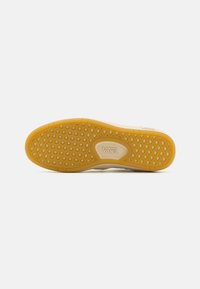 Gummisåle med sekskantet mønster, en beige base og en brunsfarget bunn. "VANS" logo preget nær hælen.