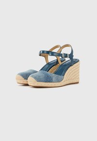 Μπλε τζιν πλατφόρμες με τακούνι περιτυλιγμένο σε σκοινί τζούτ, λουράκι αστραγάλου με ασημένιο αγκράφα και λείες δερμάτινες λεπτομέρειες.