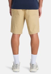 Pantaloni corti khaki, in cotone, vestibilità casual, design semplice, con orlo dritto. Indossati con calzettoni bianchi e sneakers grigio chiaro.