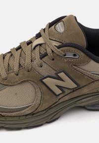 Brune semsket og mesh joggesko med polstret krage, teksturerte detaljer, tykk snøring og en fremtredende 'N'-logo i mørkegrå.