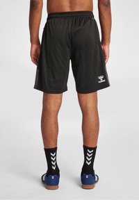 Svarta sportshorts med elastisk midjeband, tillverkade av andningsbart meshtyg. Märkbart märke på högra sidan. Kombineras med svarta strumpor och blåa skor.