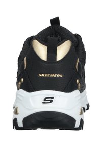 Shoe atlético preto com um cabedal texturizado, detalhes em dourado no calcanhar e sola branca. Possui uma alça de puxar e o logótipo "SKECHERS".
