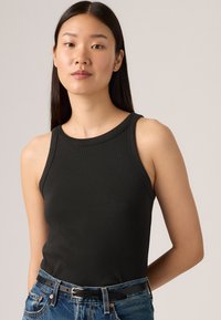 Svart ribbet tanktop med rund hals, ermeles design, kombinert med høyt liv denim og et smalt svart belte.