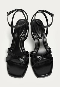 Schwarze Riemchensandalen mit eckiger Zehenpartie, glattem synthetischem Material und Knöchelriemen mit verstellbaren Schnallen.