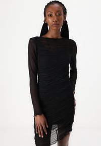 Mustasang musta na may ruched na disenyo, mahahabang sheer na manggas, asymmetrical na hemline, at textured na tela, na lumilikha ng layered na hitsura.