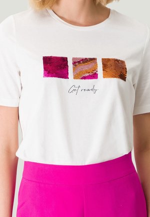T-shirt blanc avec trois carrés de sequins colorés et texte « Get ready », porté avec un pantalon taille haute rose vif.
