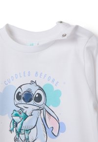 Witte T-shirt met korte mouwen, gemaakt van katoen, met een kleurrijke print van een personage dat een kikker vasthoudt, met drukknoopjes op de schouder.