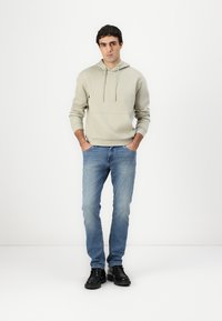 Sweatshirt com capuz em cinzento claro, com um bolso na frente e cordões, emparelhado com jeans de ganga azul e sapatos pretos com atacadores.