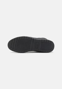 Black rubber shoe sole with a textured pattern, featuring horizontal and vertical grooves for grip. Durable material with a smooth finish.