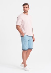 Světle růžové tričko s kulatým výstřihem v kombinaci se světle modrými šortkami s džínovými manžetami, doplněné bílými teniskami. Jednoduchý, neformální design.