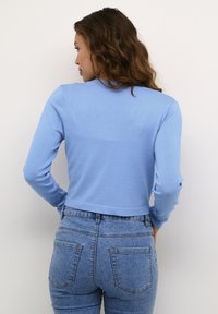 Világoskék cropped pulóver hosszú ujjal, sima textúrával, kerek nyakkal és bordázott szegéllyel, magasan derékig érő farmernadrággal párosítva.