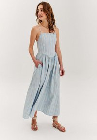 Paskowana niebieska sukienka maxi z dopasowaną górą, rozszerzanym dołem i kieszeniami; wykonana z lekkiego materiału; cienkie ramiączka.