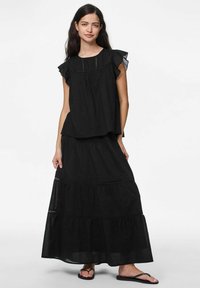 Completo nero composto da un top a maniche corte con volant e una gonna lunga fluente con dettagli in pizzo e design a strati.